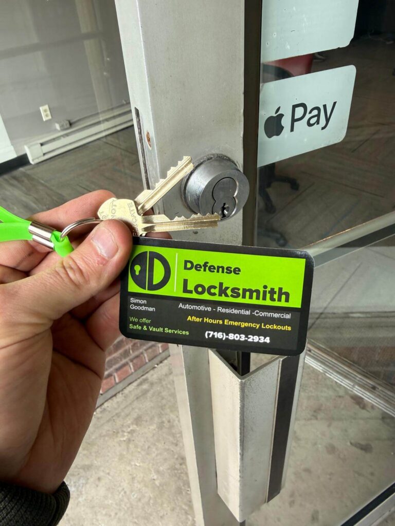 Defense Locksmith branded key tag and keys held in front of a commercial glass door in Buffalo, NY