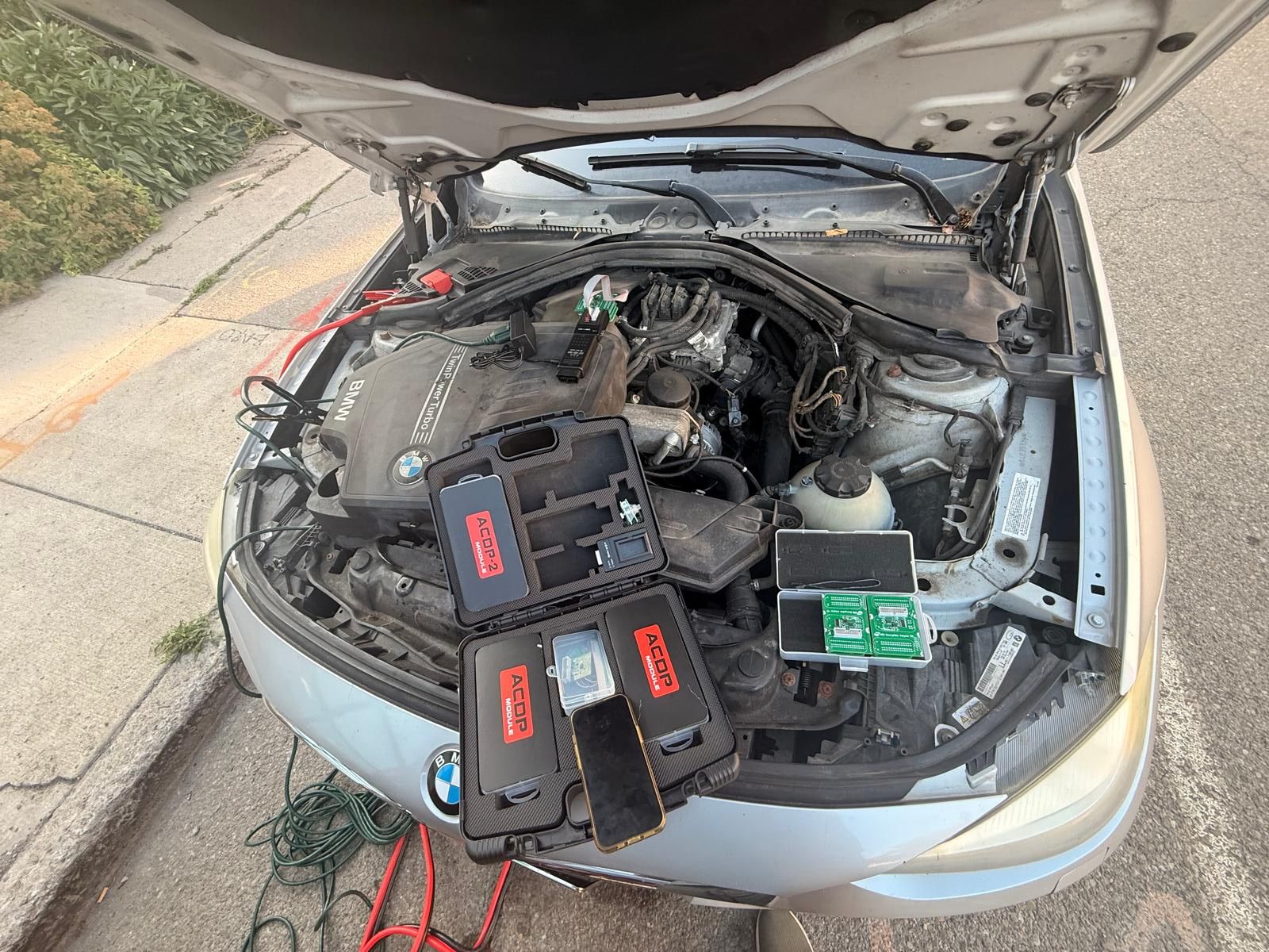 Reading a BMW ISN from the DME / ECU in Buffalo, NY BMW engine bay with the hood open and ACDP programming modules connected to the DME to read the ISN code