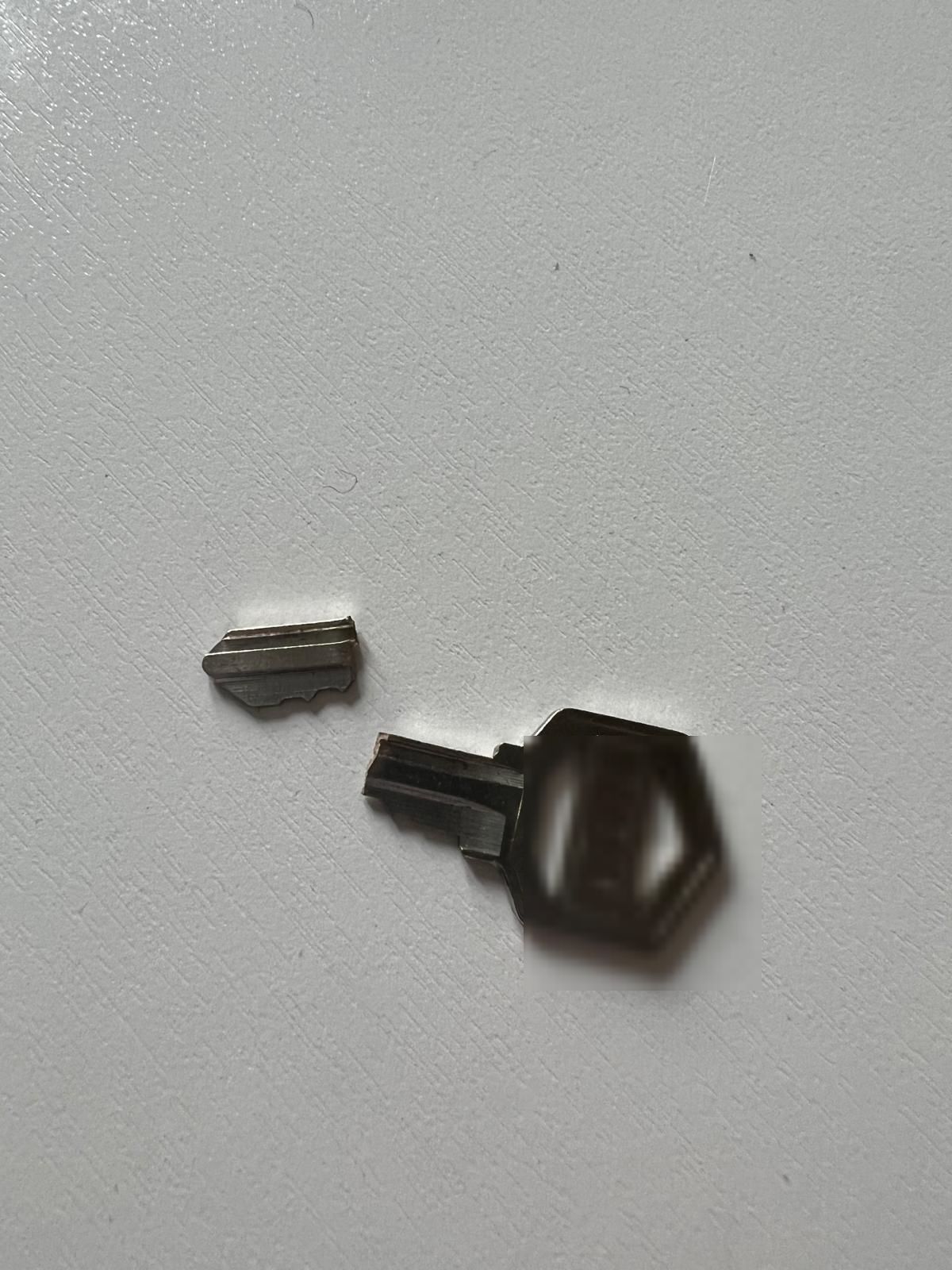 New key cut from both halves of a broken key in Buffalo, NY Two pieces of a broken key beside a freshly cut replacement, key code redacted for security